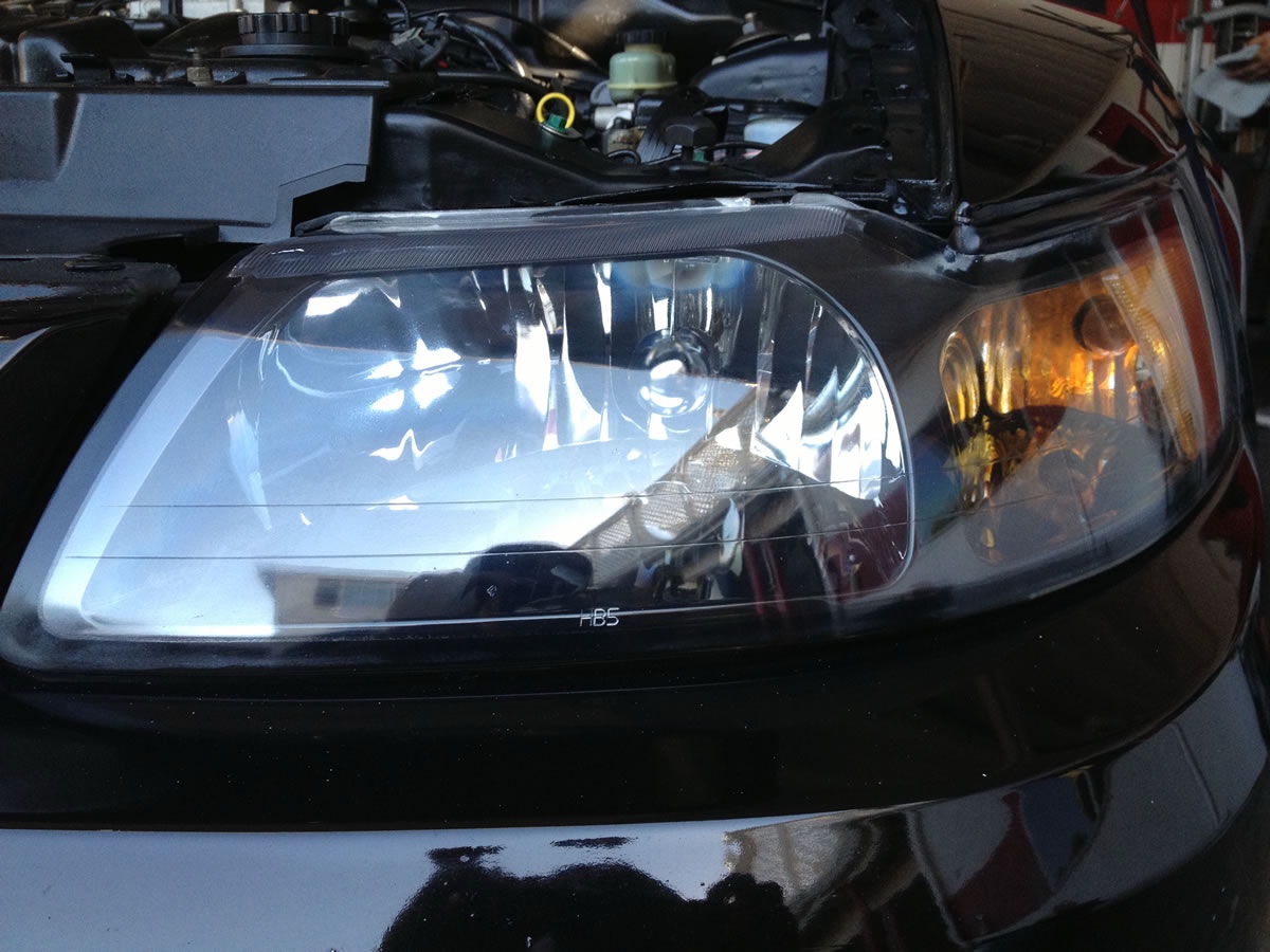 Fully restored headlight on black sedan — full optical clarity restored, internal reflector visible