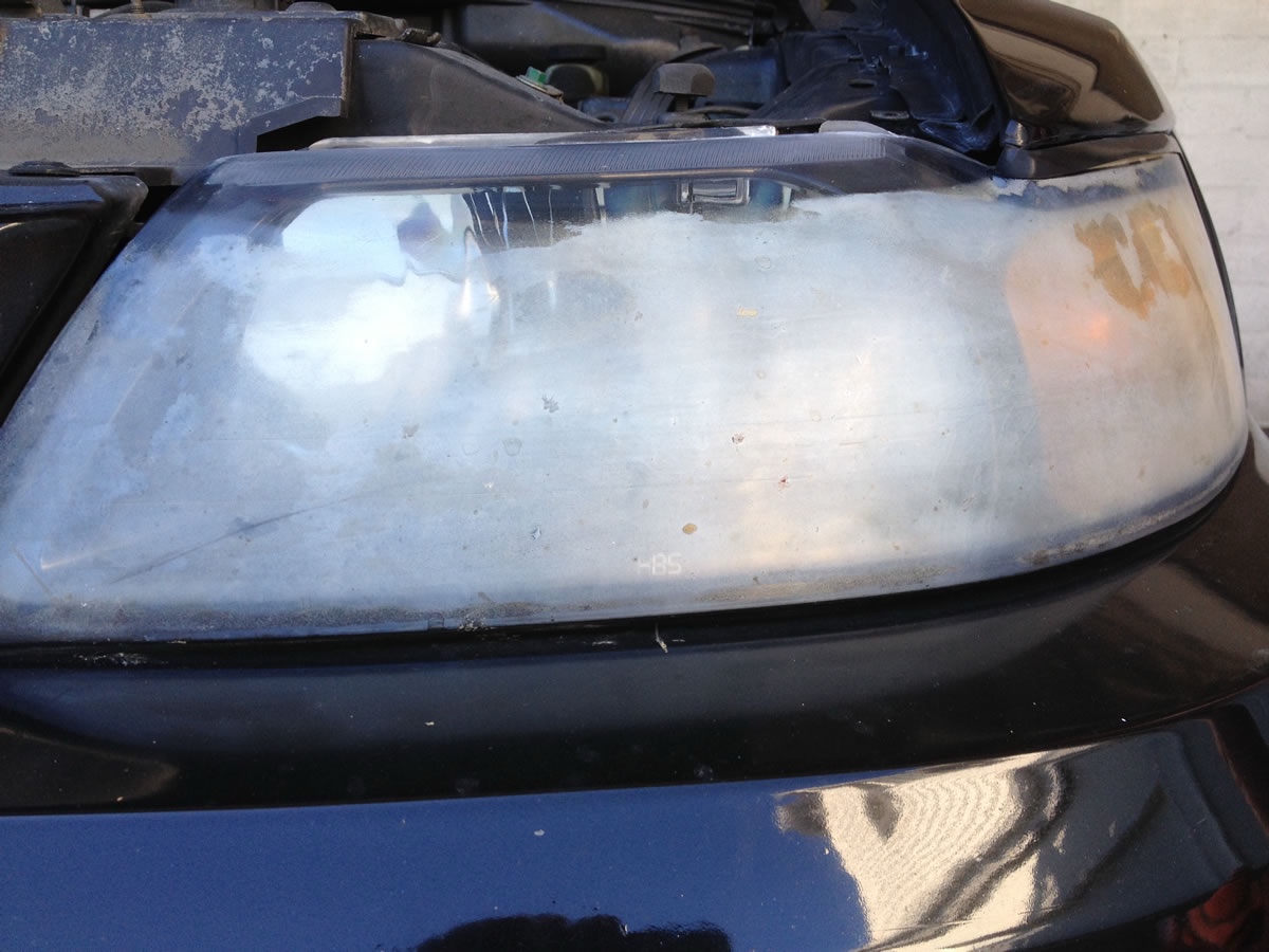 Same black sedan headlight before restoration — severe UV oxidation with milky white haze across the lens